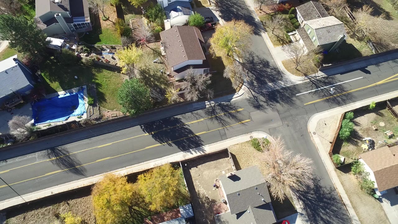 Overhead view of a residential road crossing a side street beside homes and trees.
