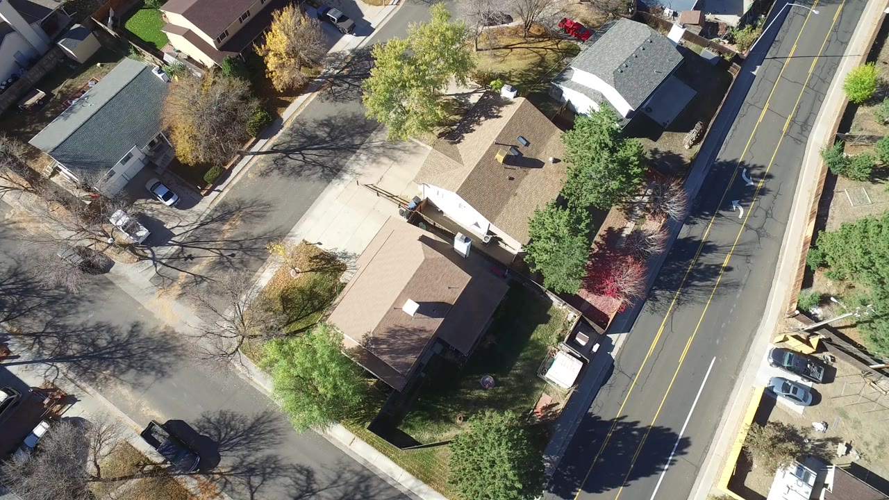 Overhead view of houses, trees, driveways, parked cars, and a two-lane road.