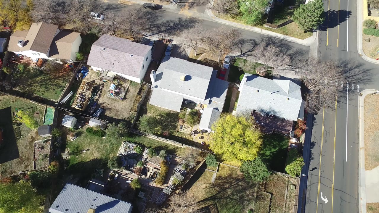 Top-down aerial frame over Hidden Lake, Colorado, showing detached homes, fenced yards, bare trees, a bright green tree, and a two-lane road at the right with no visible people.