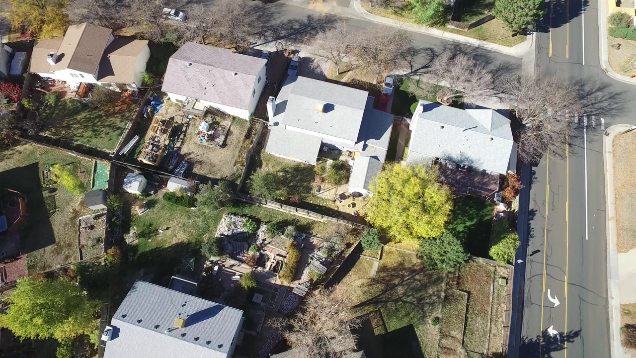 Overhead view of homes, yards, trees, and a marked road.
