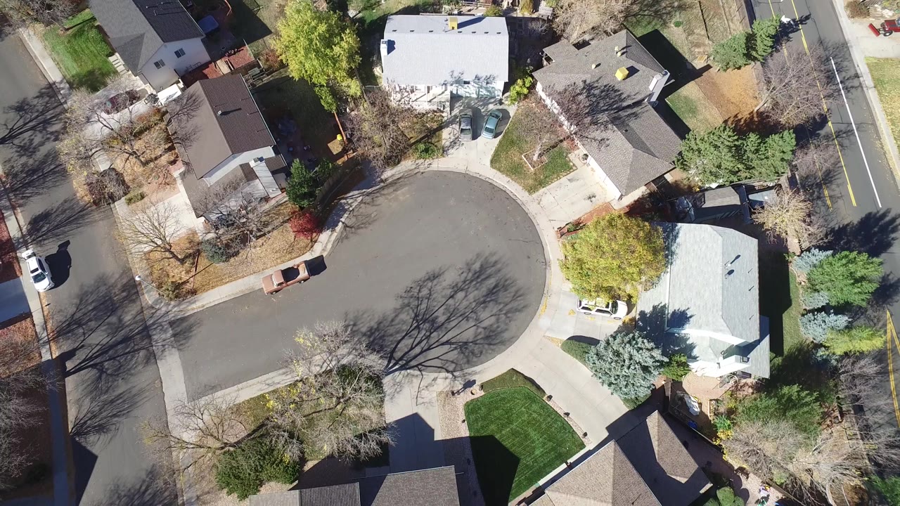 Aerial frame looking down on the same Hidden Lake, Colorado cul-de-sac, with a pale-roofed home on the right, lawns, leafless trees, and no visible people.