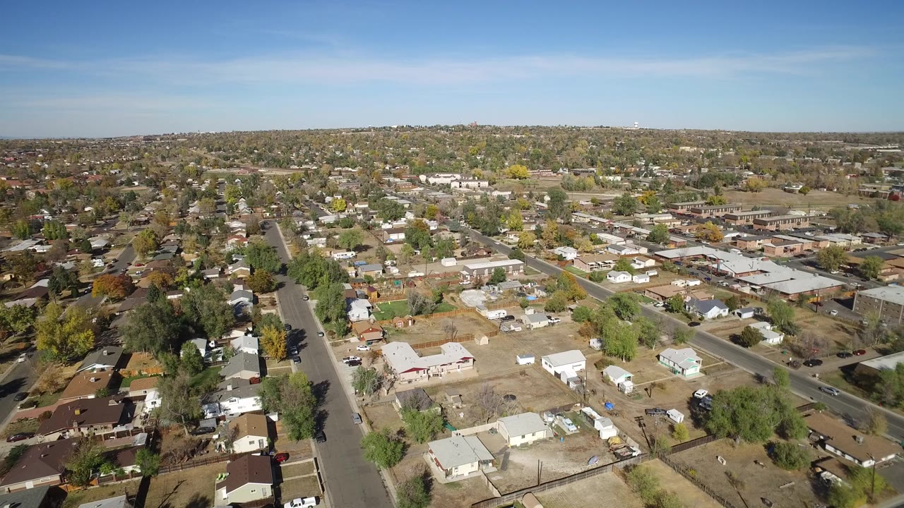 Aerial view over homes, streets, yards, and trees under blue sky.
