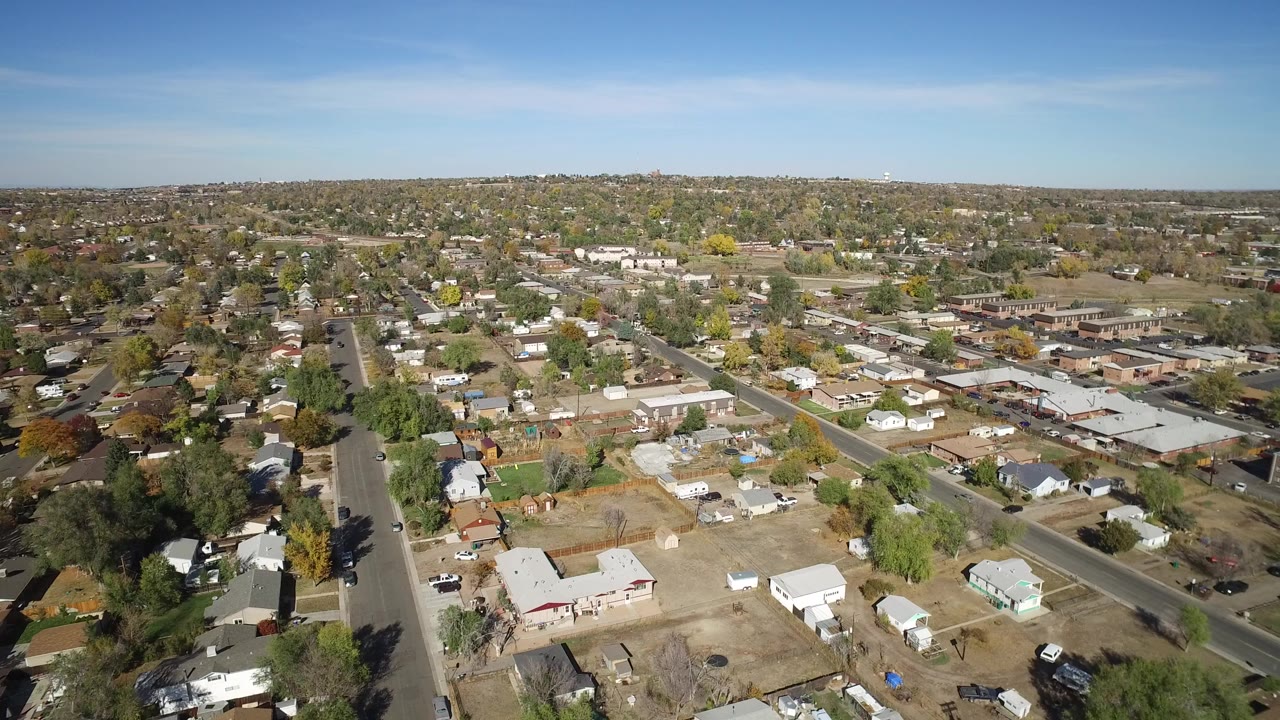 Aerial view over a residential neighborhood with streets, houses, trees, and open lots.