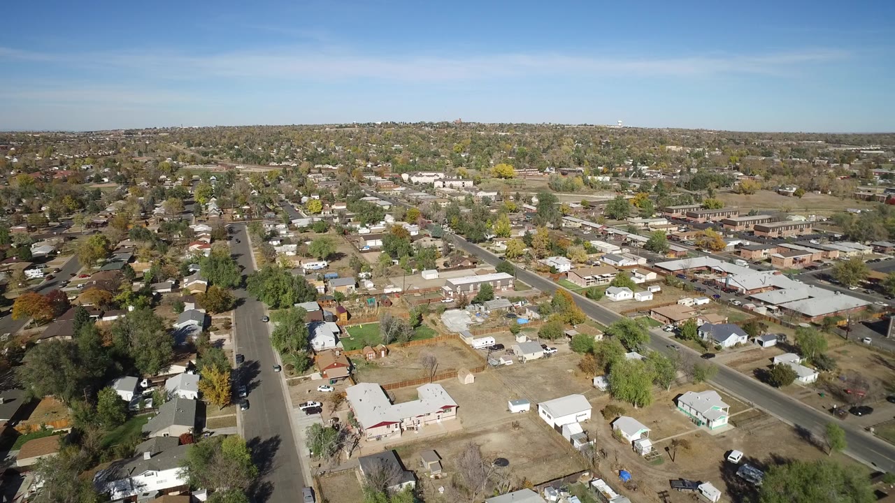 Aerial frame of Hidden Lake, Colorado looking across rooftops, tree-lined streets, small open parcels, a low building cluster, and a flat horizon with no visible people.