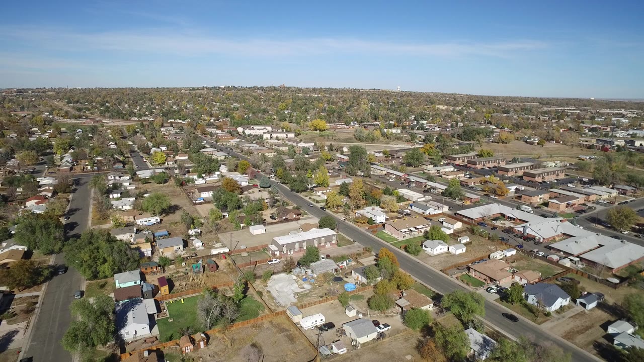 High aerial view of a residential area with roads, rooftops, trees, and blue sky.
