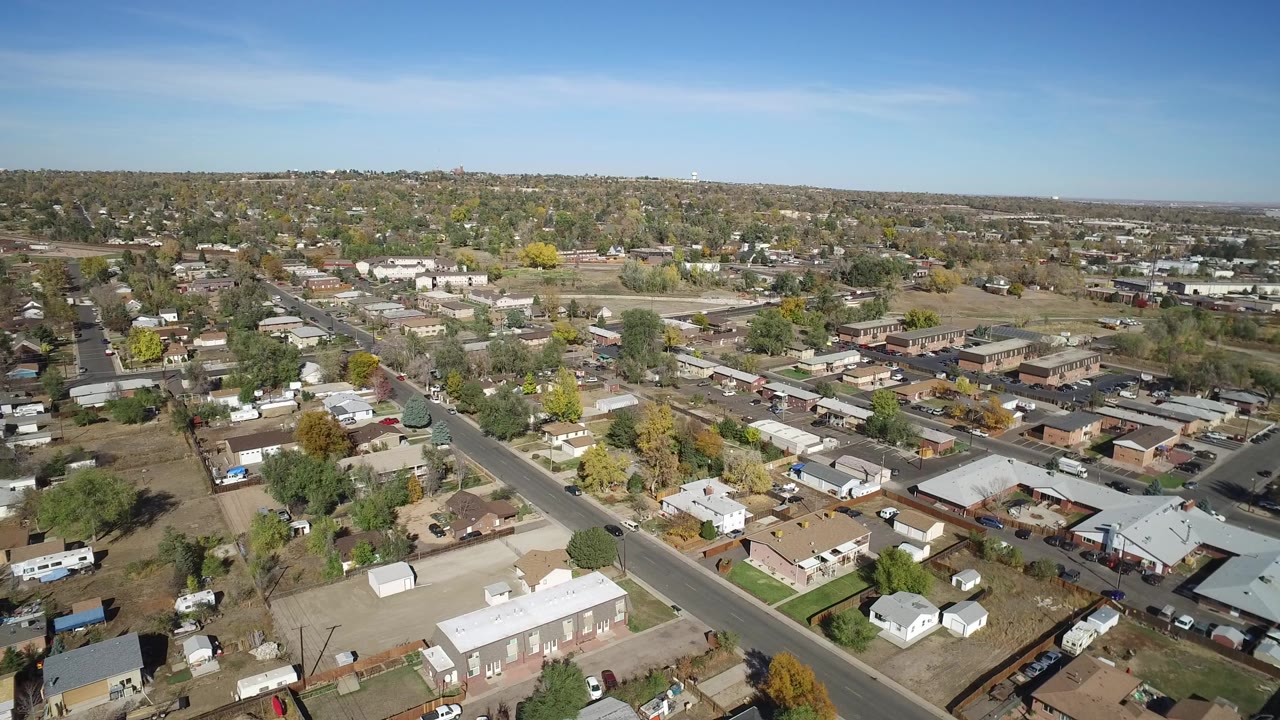 Aerial view over suburban homes, streets, trees, and blue sky.