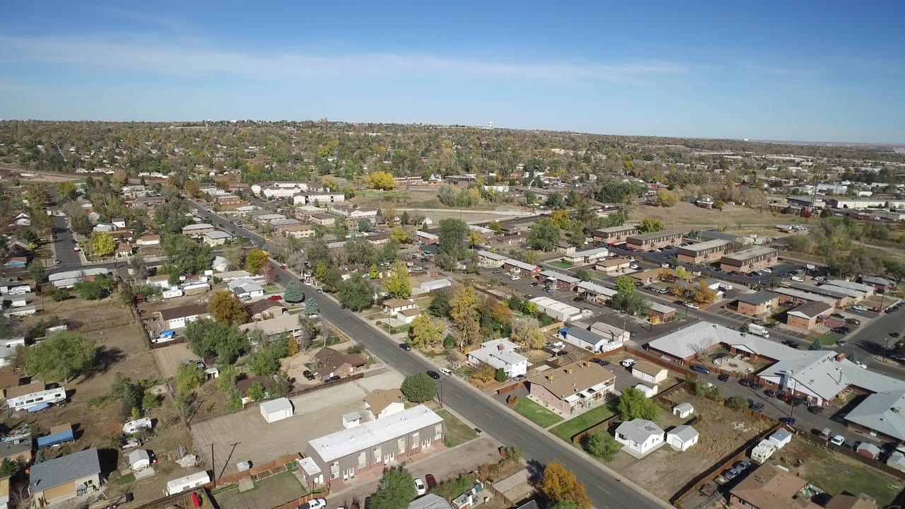 A second aerial frame in Hidden Lake, Colorado shows the neighborhood grid with rooftops, fenced yards, a diagonal road, trees, parked vehicles, and no visible people.