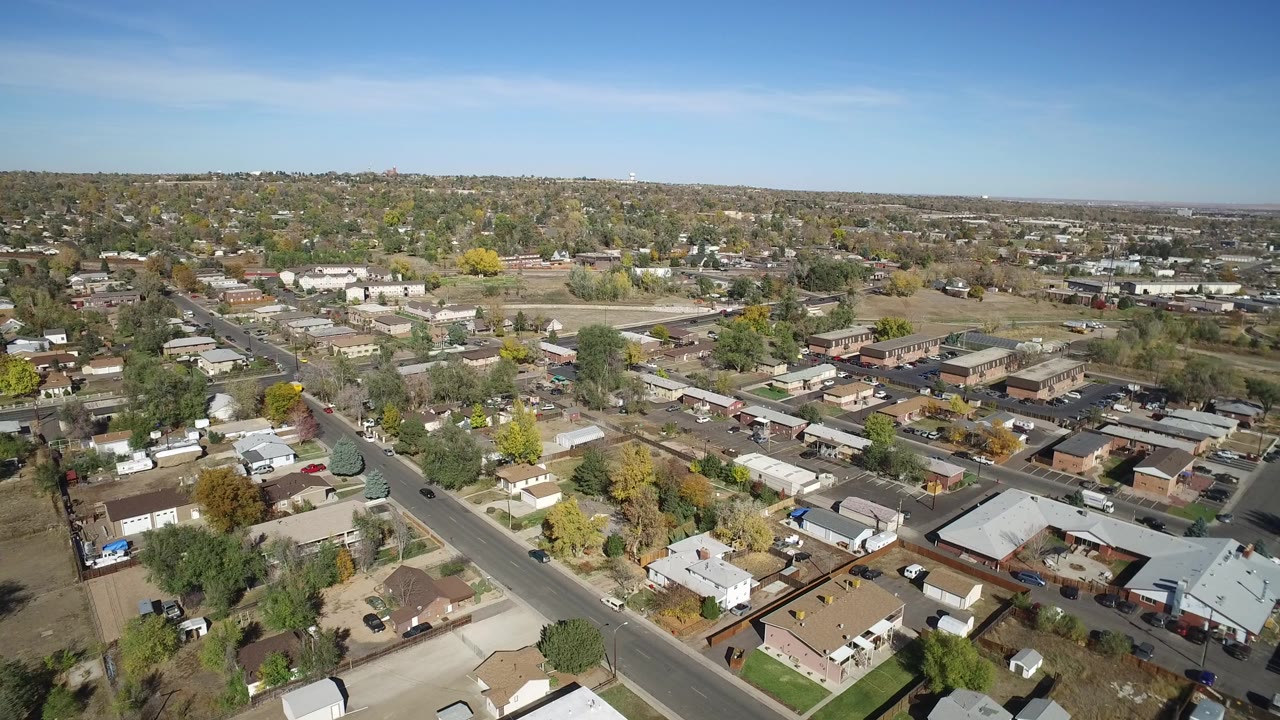 Second aerial frame over Hidden Lake Colorado showing the main road cutting through the lower left, dense rooftops, open lots, distant hills, and no visible people.