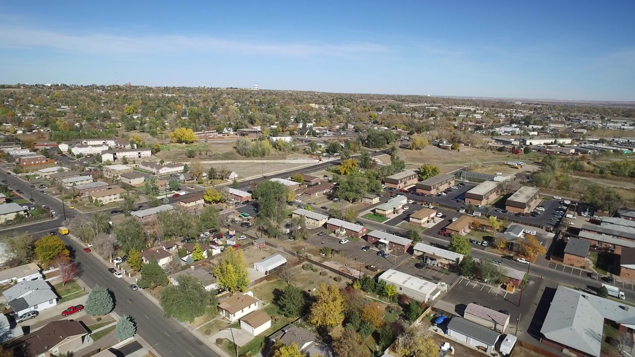 Aerial view over homes, streets, autumn trees, and low buildings under blue sky.