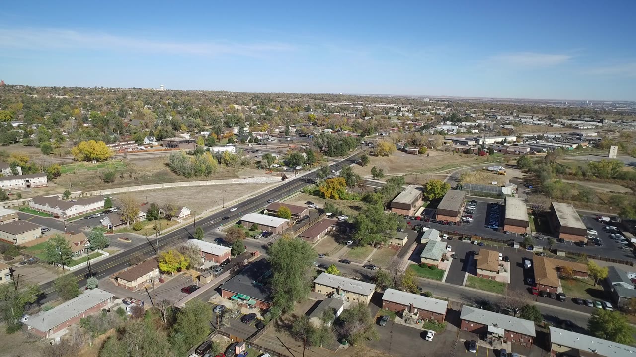 Aerial frame in Hidden Lake, Colorado, showing the main road through the midground, low buildings and homes below, autumn trees, parked cars, and no visible people.