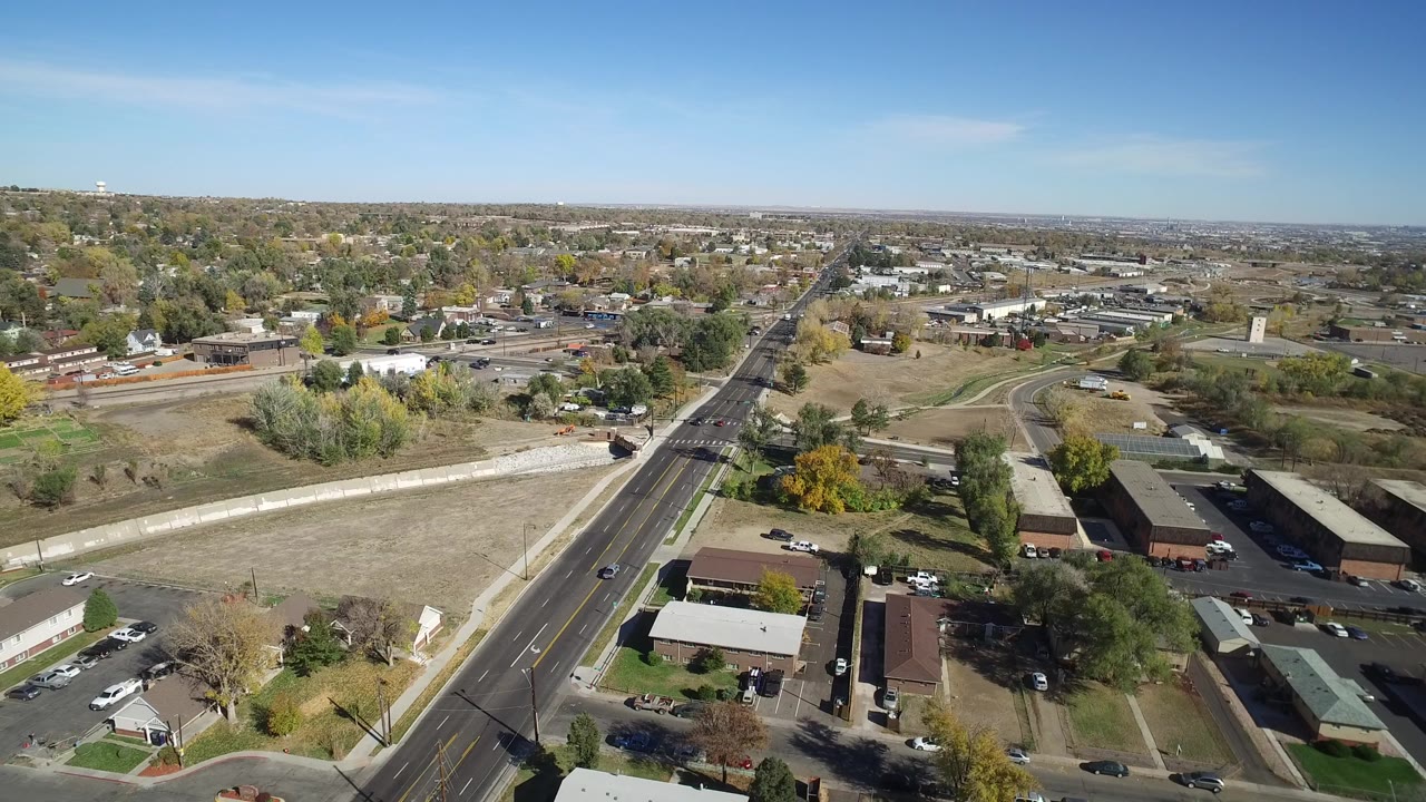 High aerial view in Hidden Lake, Colorado showing a main road, homes, low buildings, open lots, trees, and no visible people at the start of the clip.