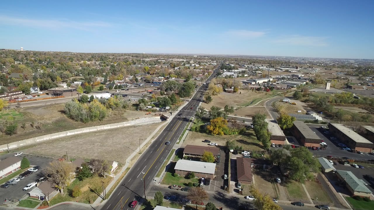 Wide aerial neighborhood view with a road, scattered trees, buildings, and cars.