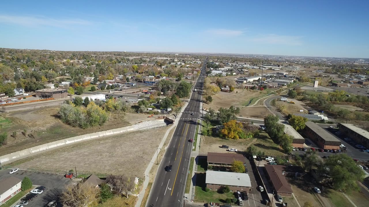 High view over a road, dry field, low buildings, and scattered autumn trees.