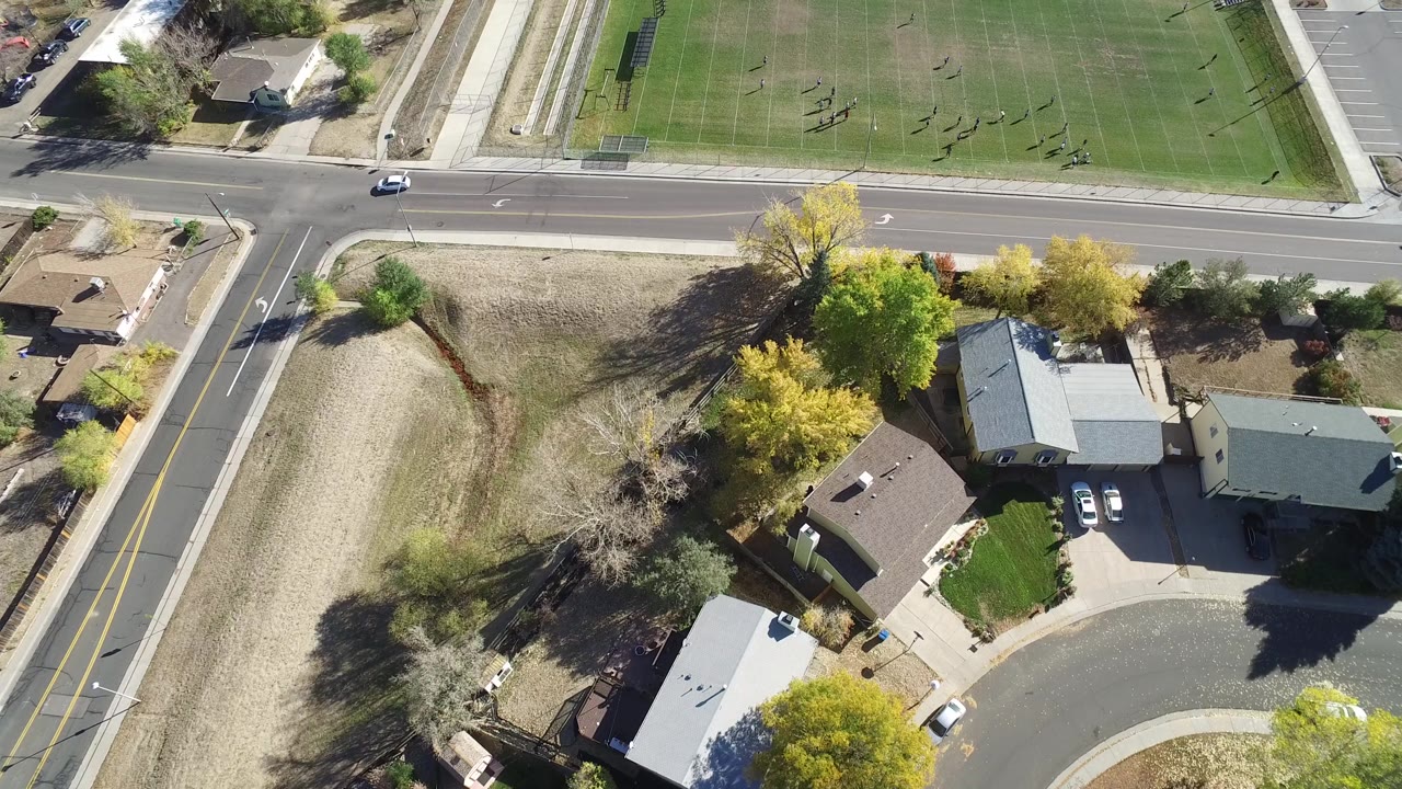 Aerial frame in Hidden Lake, Colorado with a straight road across the center, cul-de-sac houses below it, a green sports field above it, and no visible people.