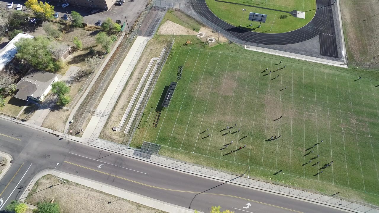 High overhead view in Hidden Lake Colorado showing a green marked sports field, a road, sidewalks, nearby buildings, trees, and small distant people with no visible faces.