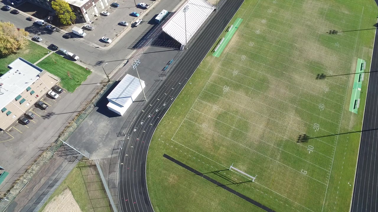Top-down view of a football field and running track beside a road and bleachers.