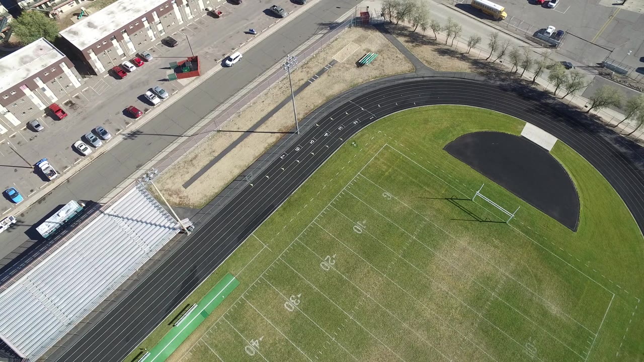 Opening overhead frame of an empty football stadium in Hidden Lake, Colorado, with the bleachers at lower left, the field and track filling the frame, and no visible people.
