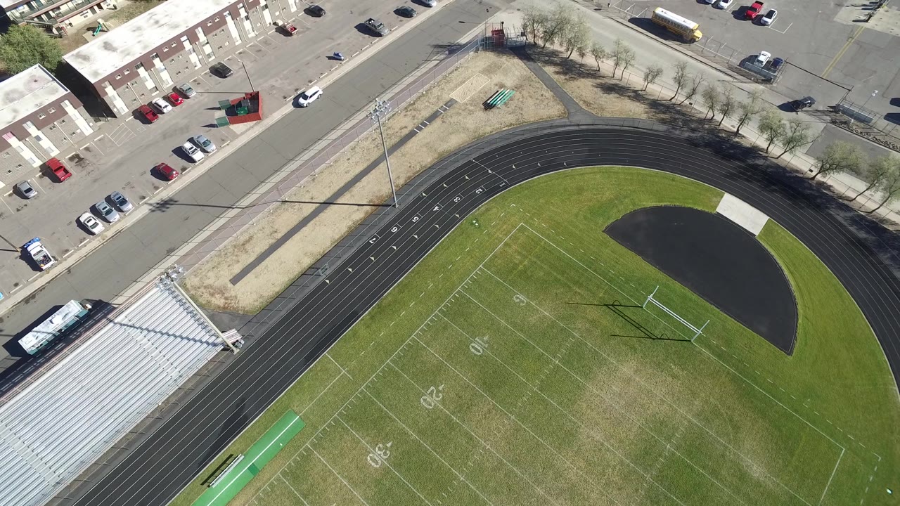 High aerial of an empty football field with track, goalpost, bleachers, and street.