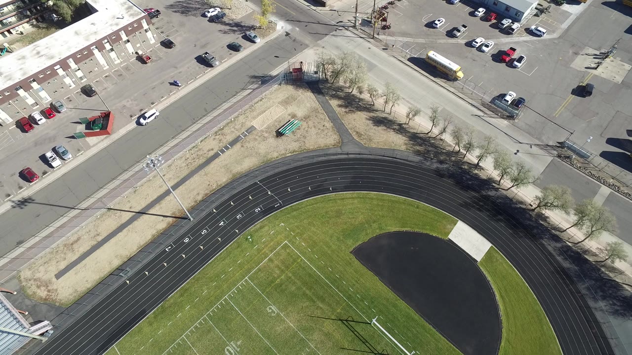 Overhead view of a track, sports field, road corner, parking lots, and industrial buildings.