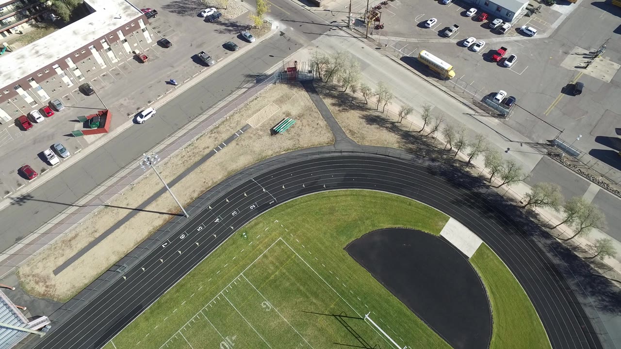 One second in, the Hidden Lake, Colorado aerial holds on the same track curve and field while the road corner, yellow bus, parked vehicles, and utility shadows remain prominent, with no visible people.