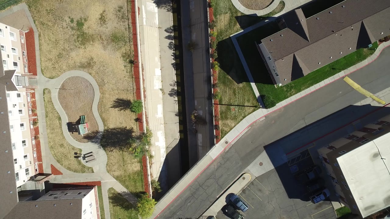 Aerial view of a curved roadway between residential buildings and open grass.