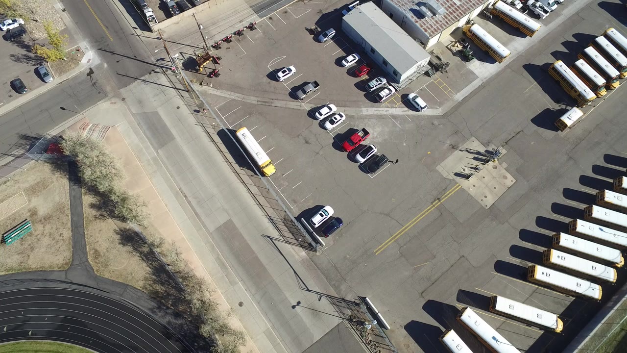 Overhead view of a commercial parking lot, road, parked cars, and buses or trailers.