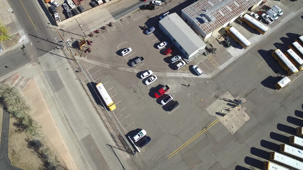 Overhead view of a warehouse lot with parked cars and yellow buses.