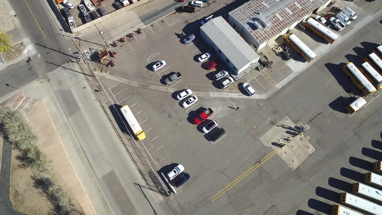 Second overhead frame in Hidden Lake, Colorado with the long warehouse roof near the top, white and red cars in the lot, yellow buses along the side, and no visible people.