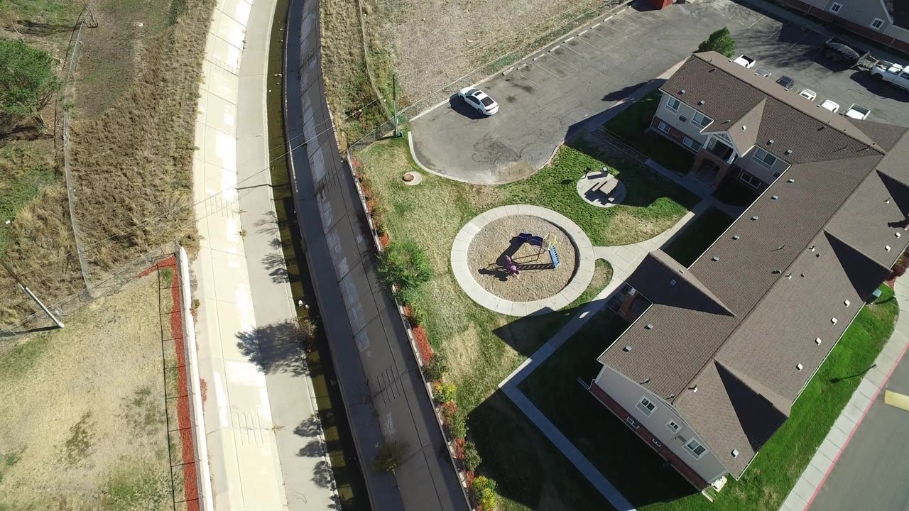 Aerial view of a brown-roofed residential building beside a curved road and playground.