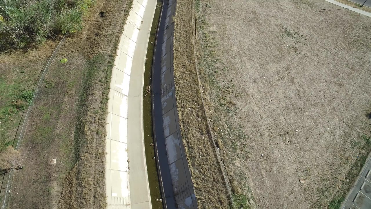 Top-down view of channel, path, dry land, shrubs, and fencing.