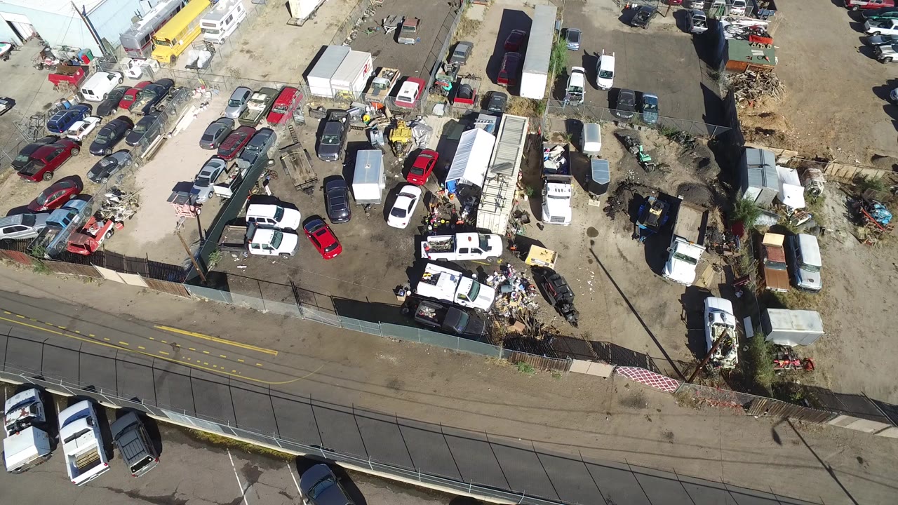 Opening overhead frame of a Hidden Lake, Colorado parking yard with clusters of cars, trailers, fencing, a two-lane road, and no visible people.