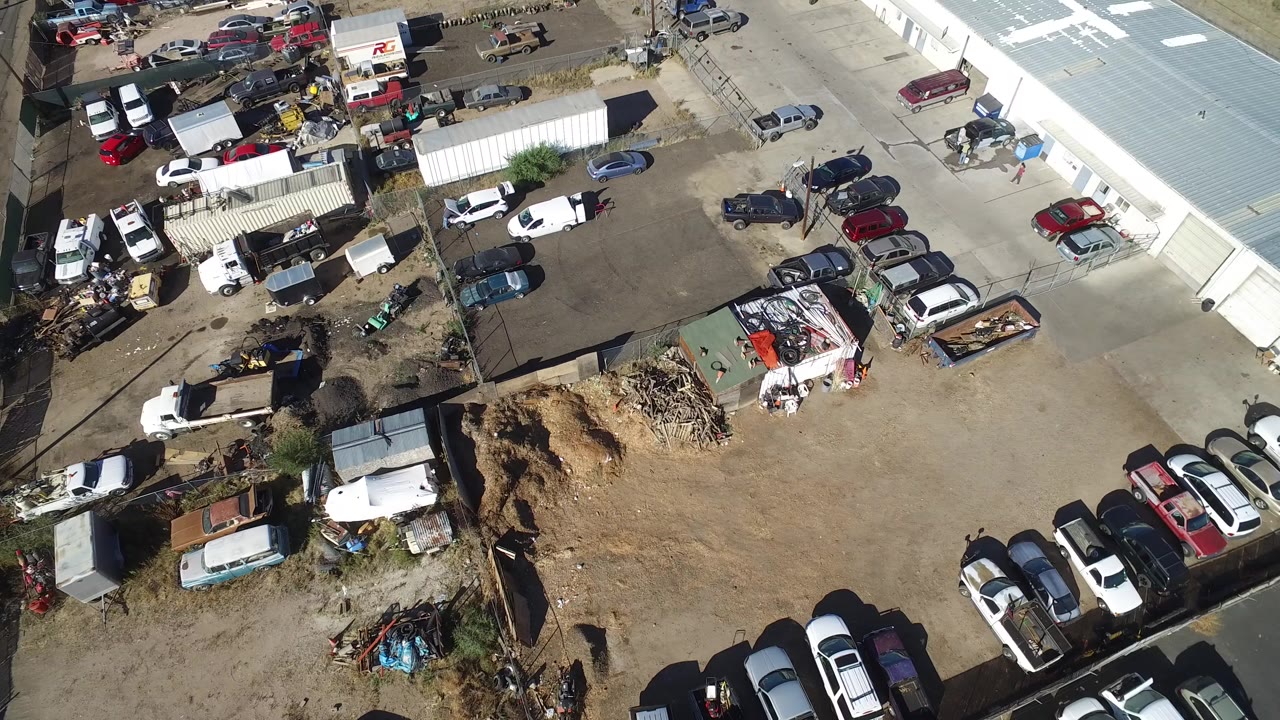 Aerial view of parked cars around a dusty warehouse lot.