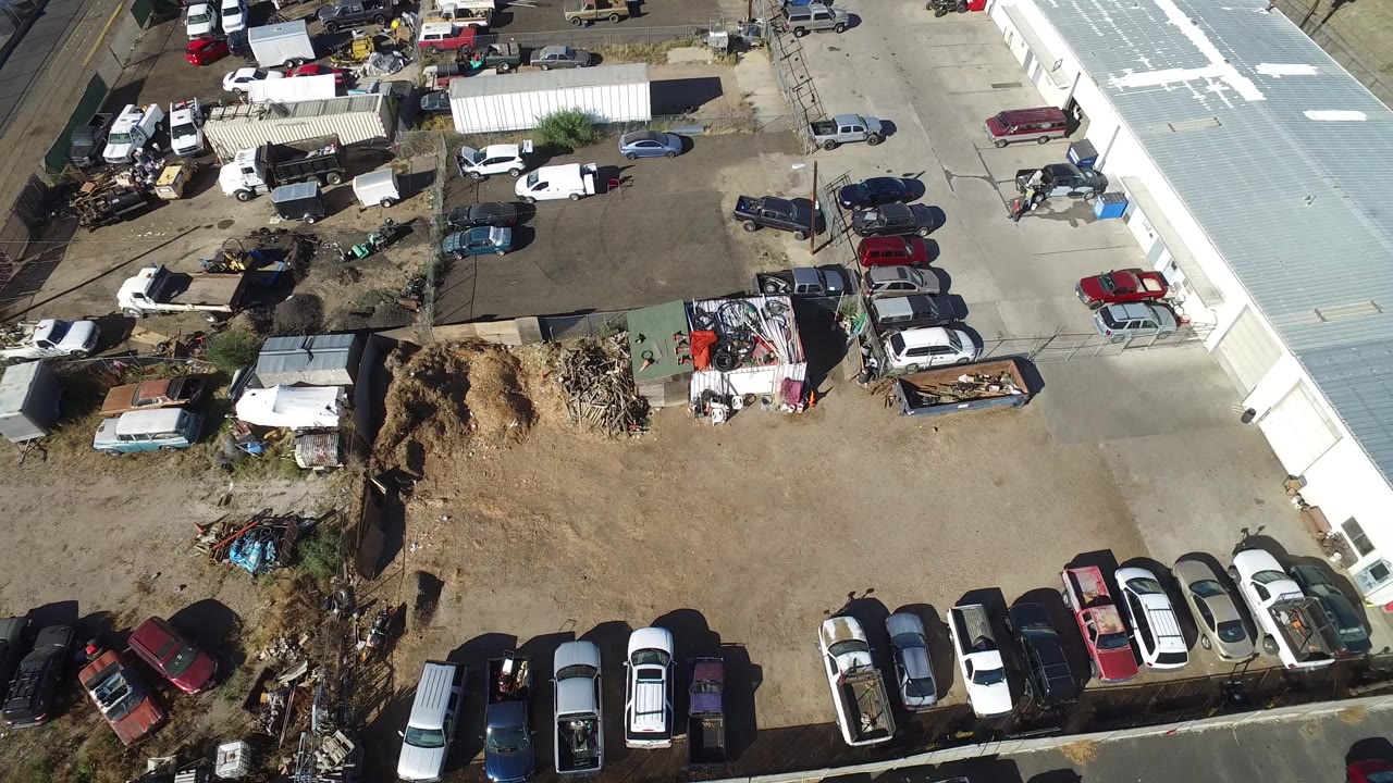 Aerial view of parked cars beside a metal-roofed building and dirt lot.