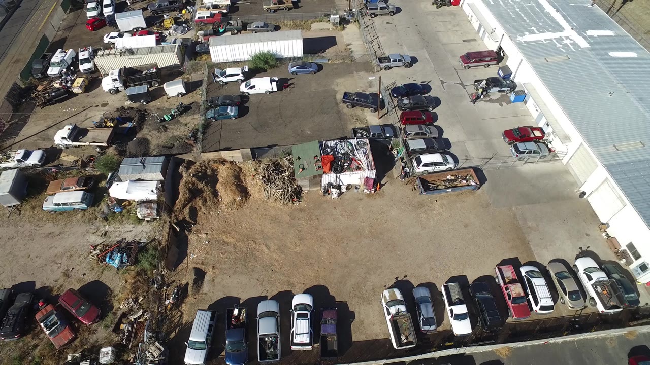 Overhead frame in Hidden Lake, Colorado with parked vehicles arranged around a mixed dirt and pavement lot, trailers near the top, and no visible people.