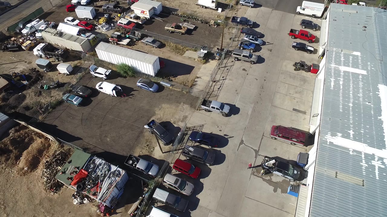 Overhead industrial yard with cars, trailers, scrap materials, and a bright metal roof edge.