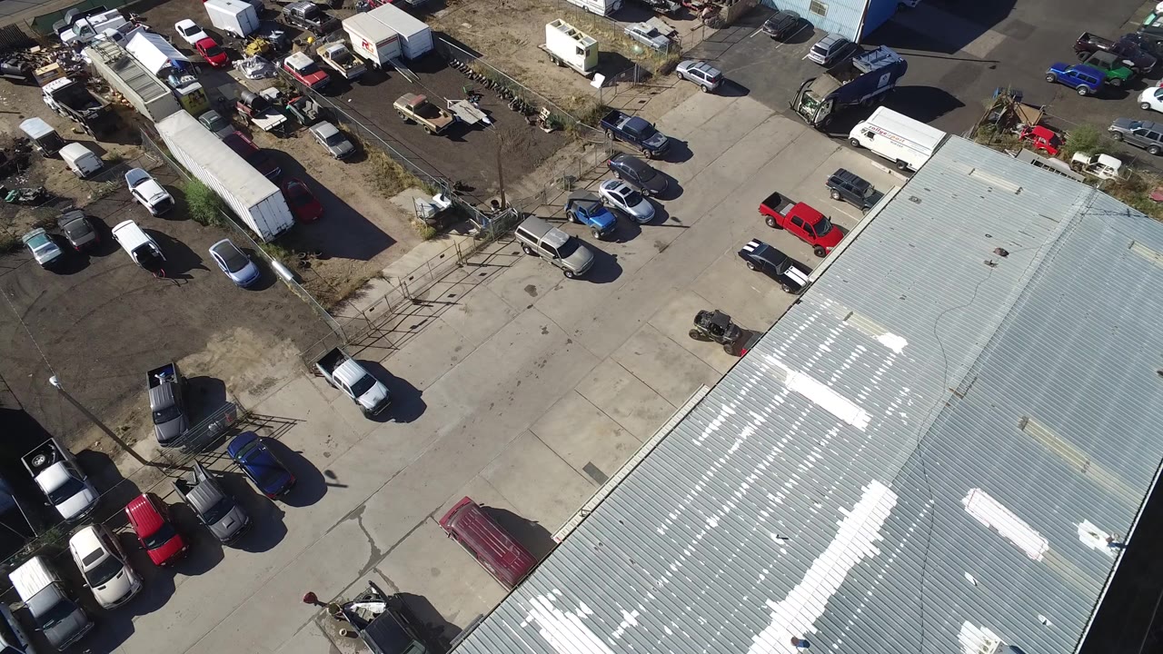 Aerial view of a metal factory roof and crowded parking lot.