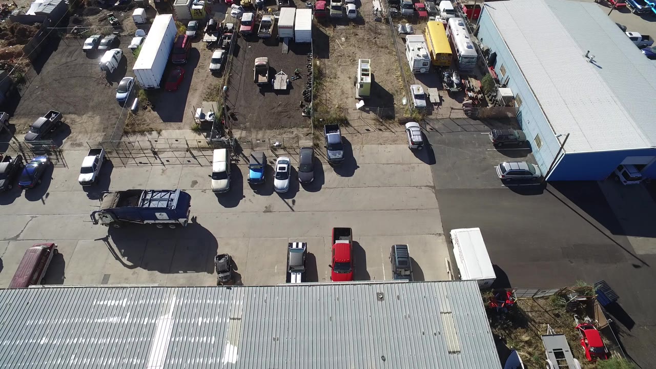 Overhead view of parked vehicles beside metal-roofed sheds and a fenced yard.