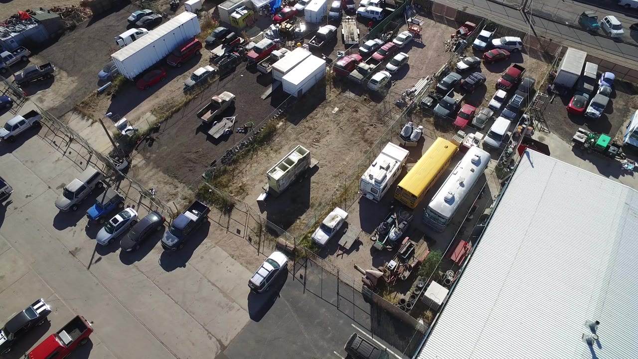 Drone-like aerial angle over a half-full junkyard with roads and parked vehicles.