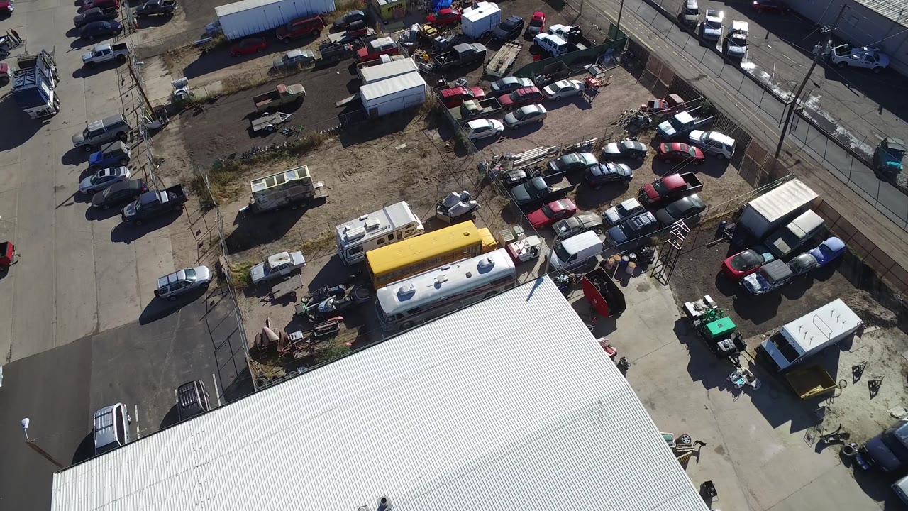 Drone-style overhead frame in Hidden Lake, Colorado, showing the white roof in the foreground, a compact parking lot with cars and trailers behind it, and no visible people.
