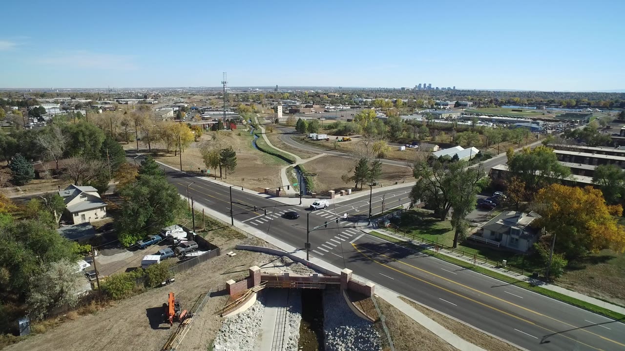 Opening aerial frame over Hidden Lake, Colorado, showing a road intersection, crosswalks, a drainage channel in the foreground, homes, trees, parked cars, and no individually visible people.