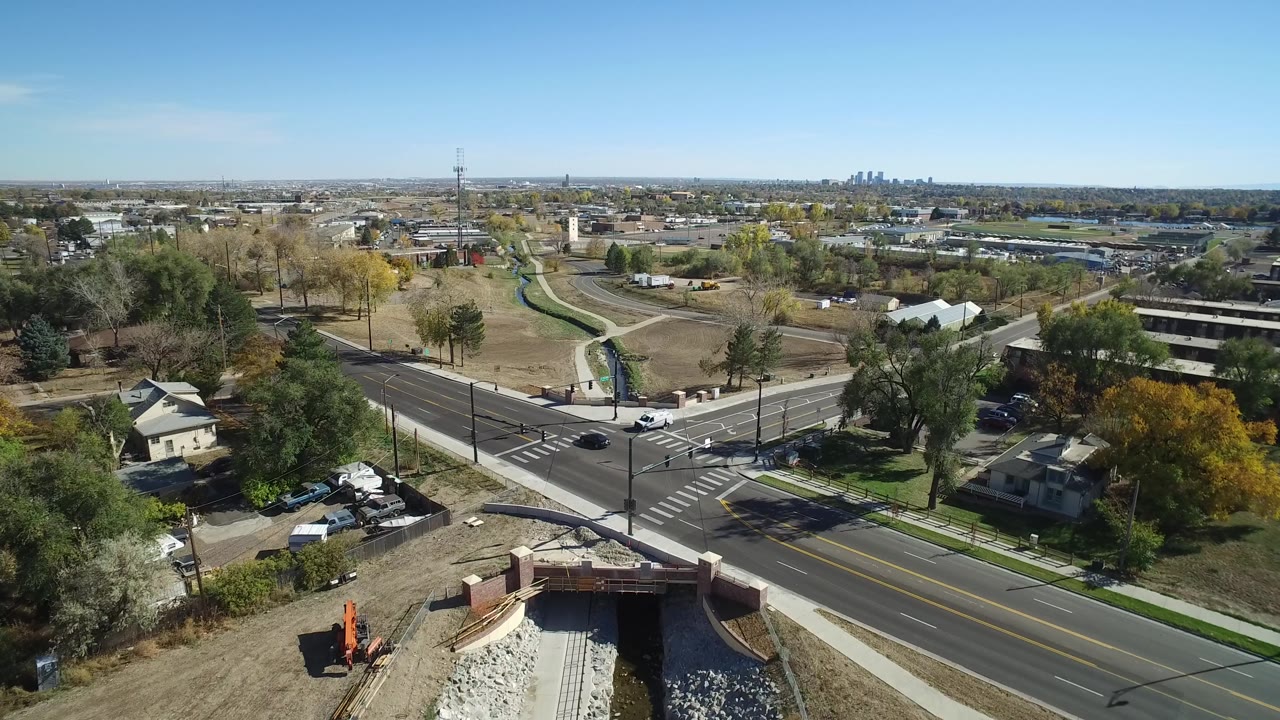 Aerial view in Hidden Lake, Colorado, centered on a multi-lane intersection with crosswalk markings, roadside trees, small houses, parked vehicles, and no individually visible people.
