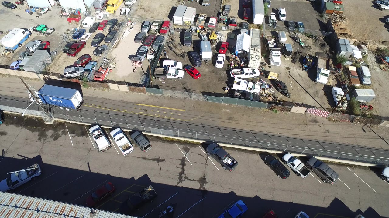 Overhead view of a white truck with a blue container on a road beside industrial lots.