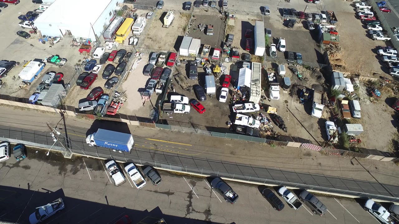 Second overhead frame in Hidden Lake, Colorado with the blue van near the lower road edge, dense rows of parked vehicles, storage trailers, and no visible people.