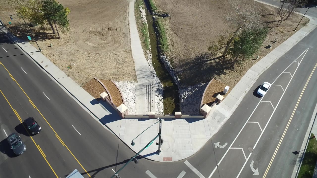 Overhead road crossing near creek, bridge, tan grass, trees, and cars.