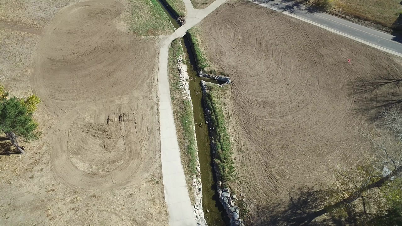 Overhead view of dirt fields, a pale path, creek, and paved road edge.