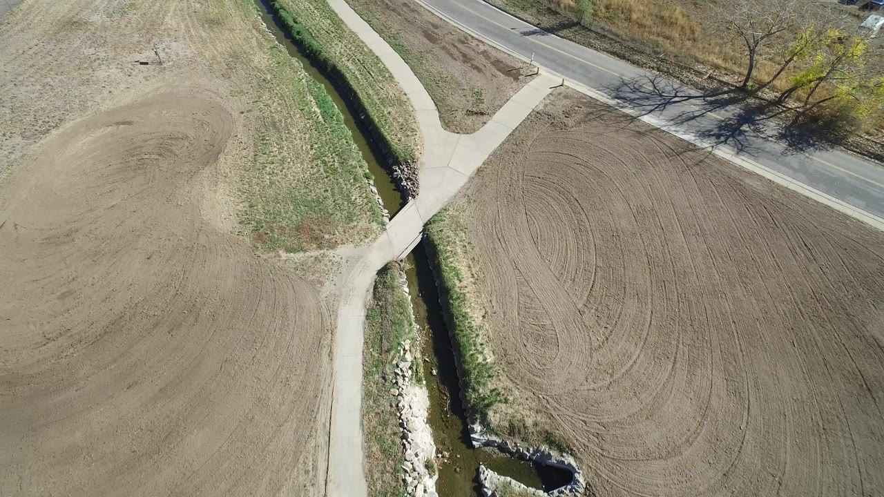 Overhead view of curved road, paths, creek, grass, and dirt field.