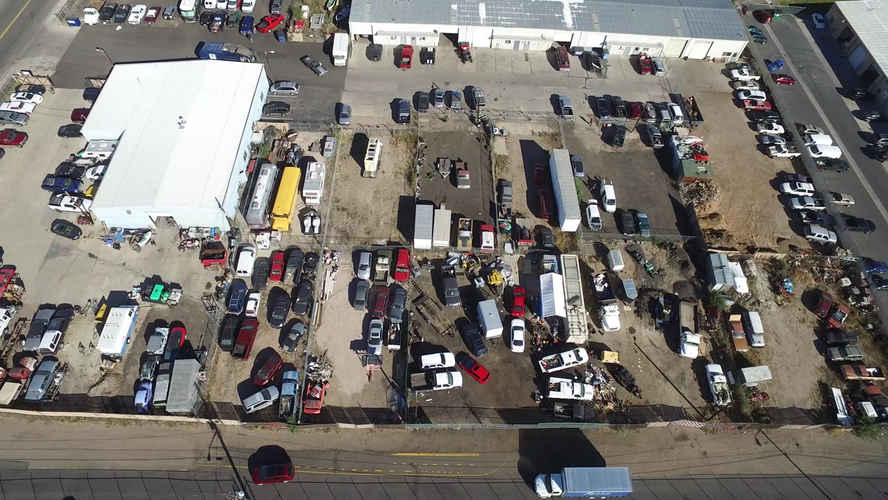 Overhead view of a white-roofed building beside a crowded parking and storage lot.