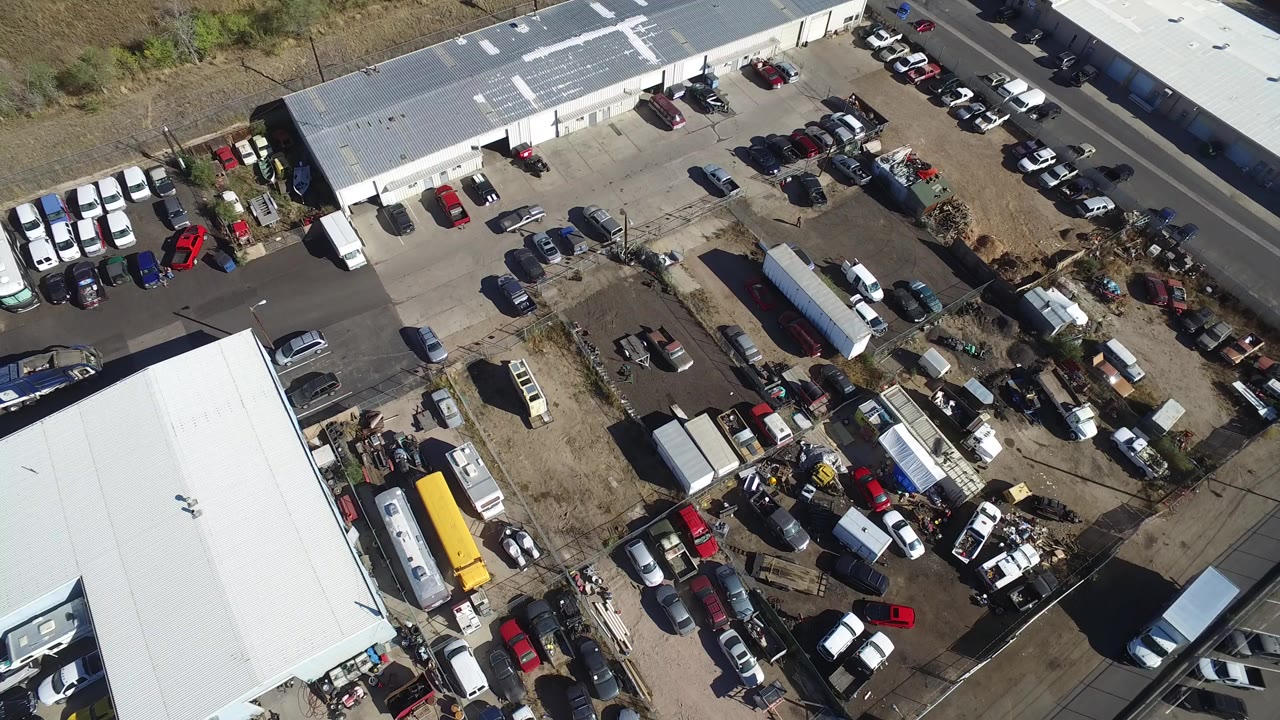 Overhead view of cars parked around warehouse buildings and a fenced yard.