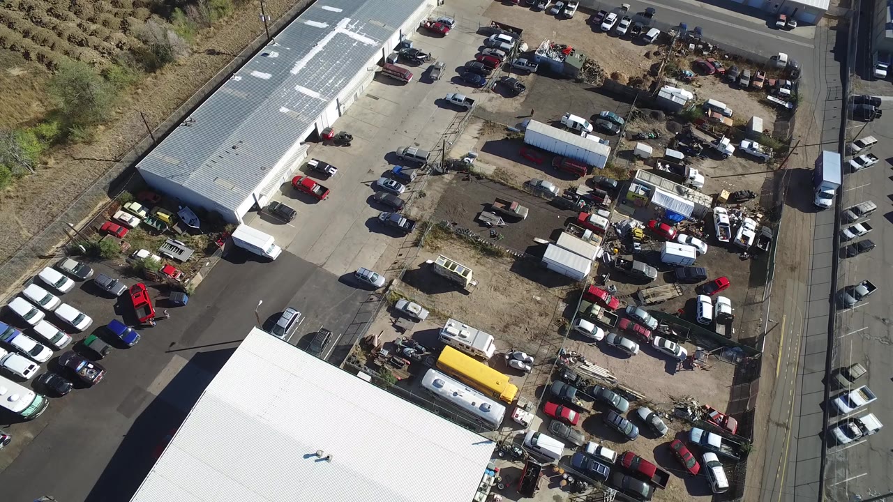A slightly shifted overhead view in Hidden Lake, Colorado shows parked cars, trucks, a yellow vehicle, storage clutter, white-roofed structures, road edges, and no visible people.