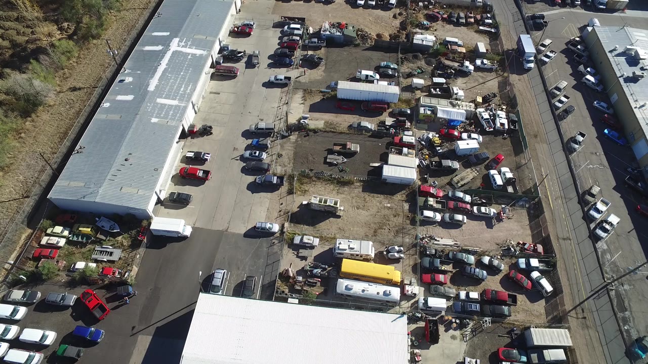 Overhead frame of the Hidden Lake parking area with rows of cars, a yellow vehicle or trailer near the lower edge, storage piles, buildings, and no visible people.